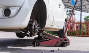 Białe Audi A6 C6 podniesione na czerwonym lewarku, widoczny hamulec i felga.