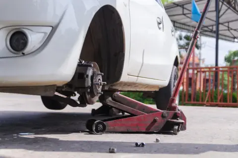 Białe Audi A6 C6 podniesione na czerwonym lewarku, widoczny hamulec i felga.